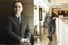 person writing in a notebook beside by an iPad, laptop, printed photos, spectacles, and a cup of coffee on a saucer